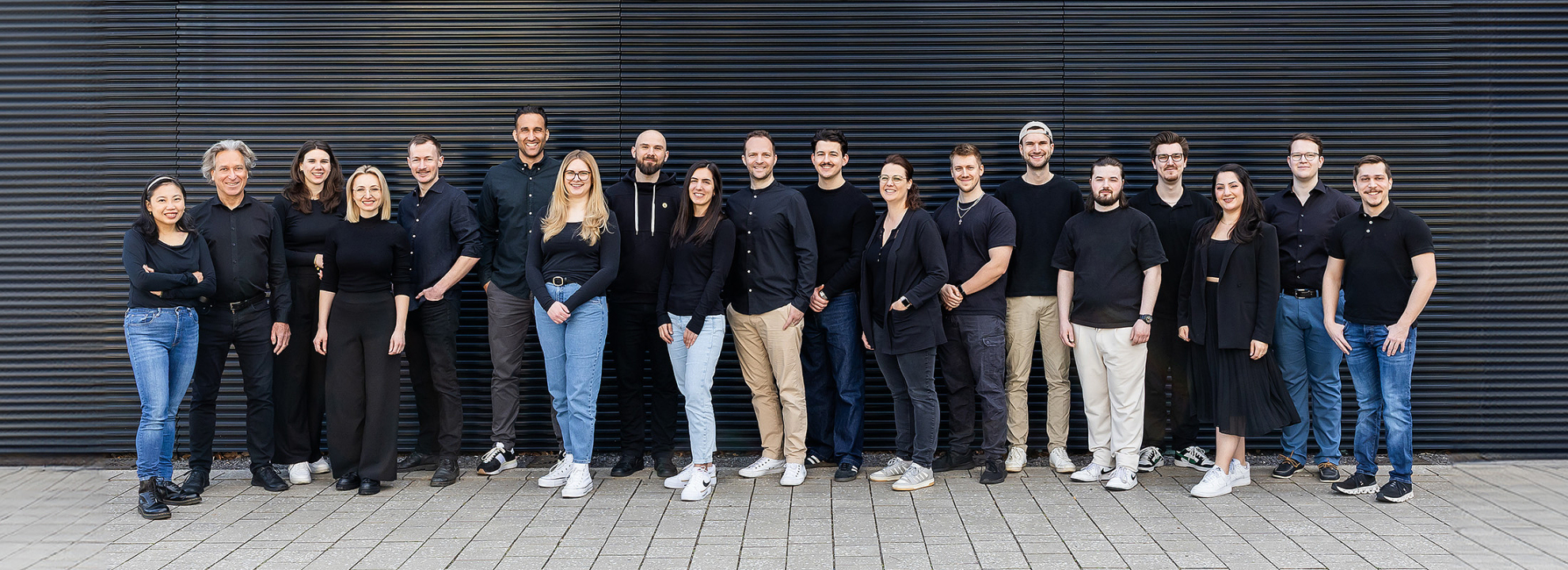 Gruppenfoto des mindtwo Teams auf einer Au&szlig;entreppe, alle in schwarzer Kleidung, l&auml;chelnd in die Kamera