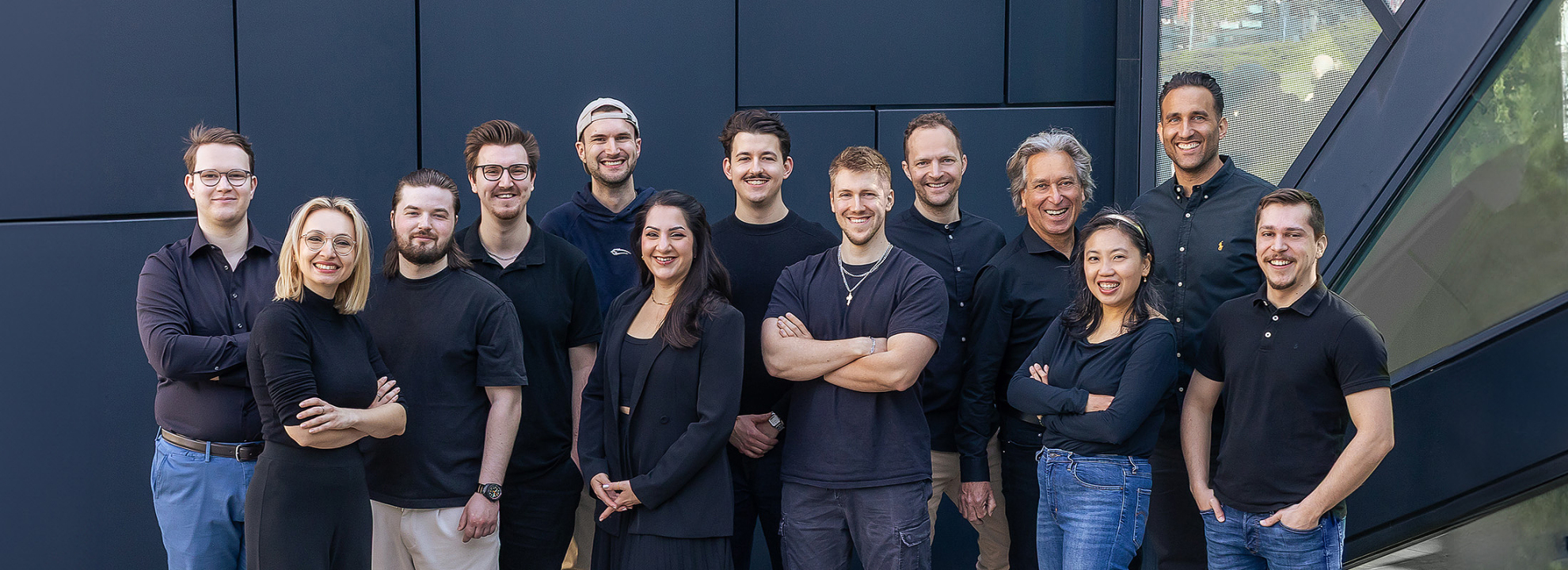 Gruppenfoto des mindtwo Teams auf einer Au&szlig;entreppe, alle in schwarzer Kleidung, l&auml;chelnd in die Kamera