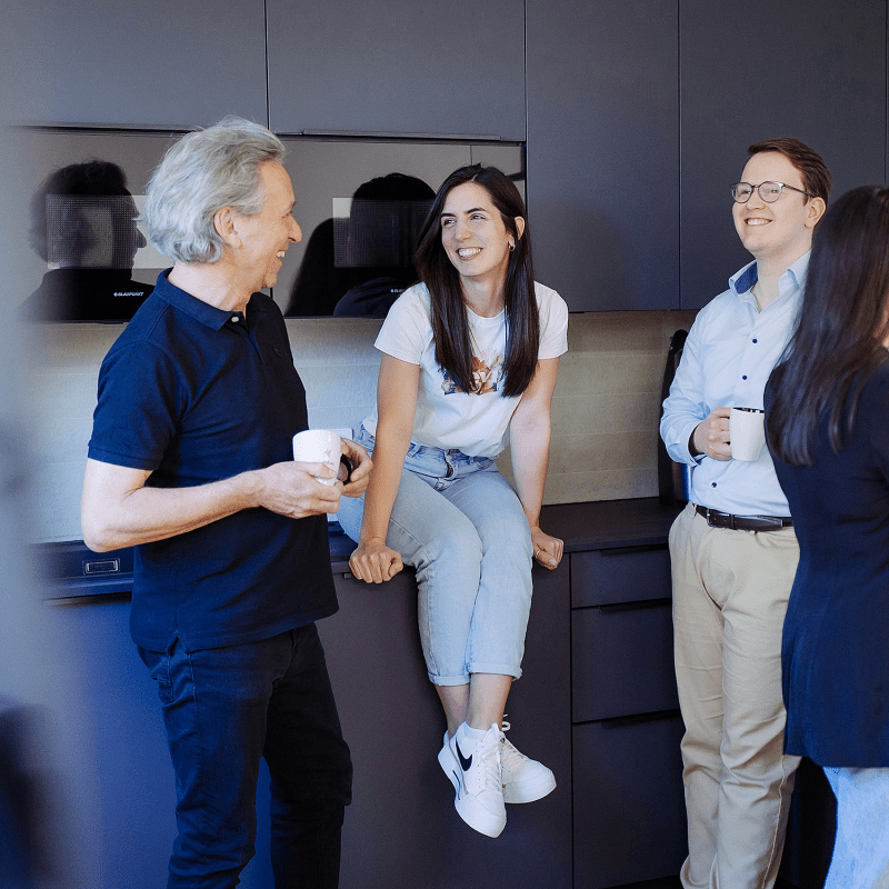 Vier Personen unterhalten sich entspannt in einer modernen Büroküche bei einer Kaffeepause.