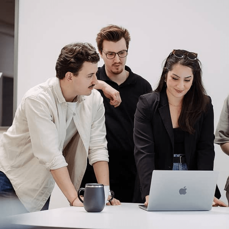 Drei mindtwo Teammitglieder bei einer Besprechung am Laptop, konzentriert und l&auml;chelnd.