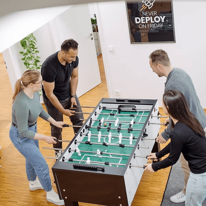Vier mindtwo Teammitglieder spielen gemeinsam Tischkicker im B&uuml;ro
