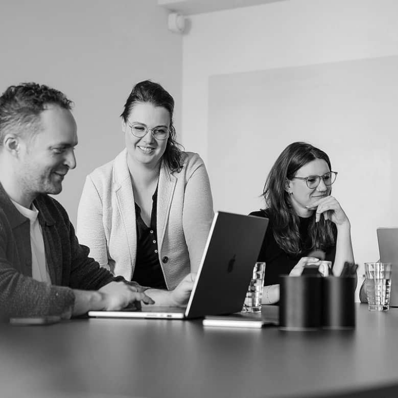 Drei Personen im Gespr&auml;ch vor Laptops bei einem Meeting in Schwarzwei&szlig;